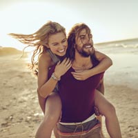 homem carregando mulher em suas costas com uma praia ao fundo